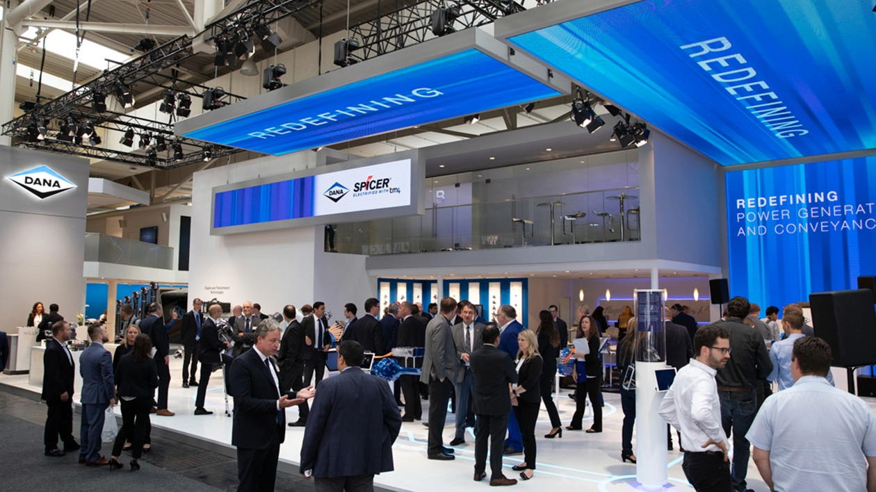 A large group of tradeshow attendees mingle among branded booths with a large Dana and Spicer booth as the focal point.