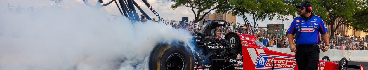 Mopar Direct Connection car in background with crew member in foreground, smoke coming from car as it revs its engine