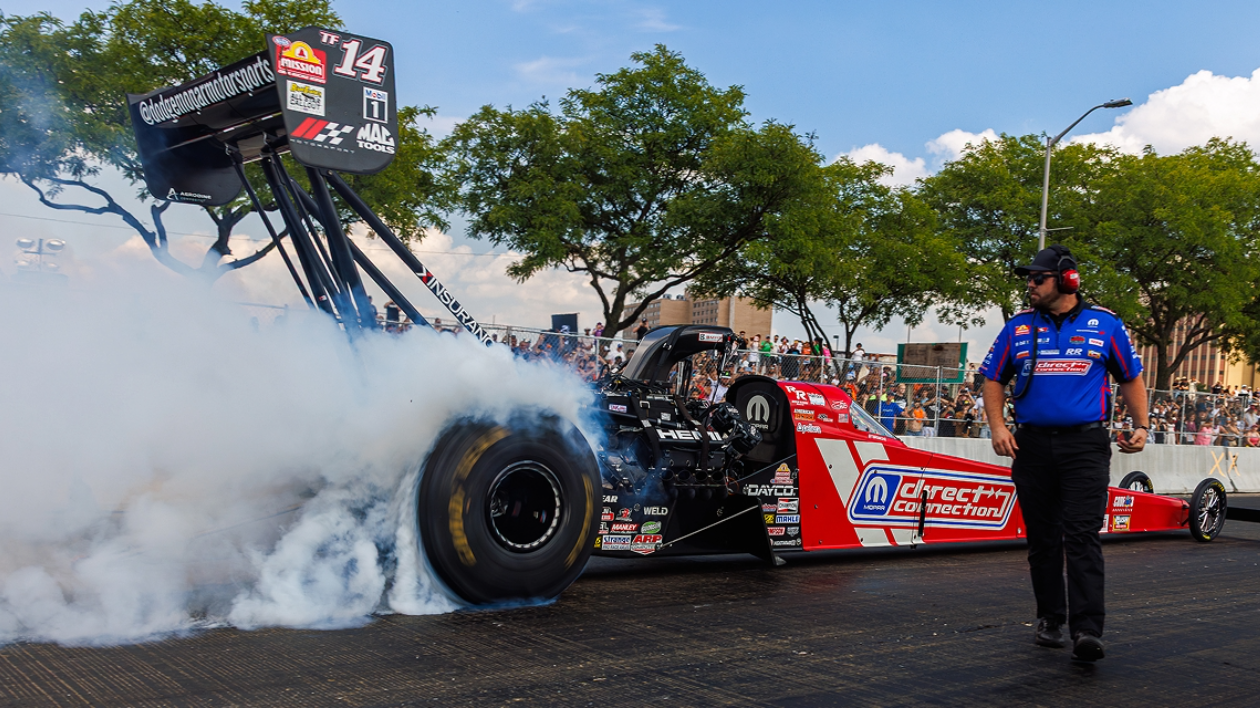 Mopar Direct Connection car in background with crew member in foreground, smoke coming from car as it revs its engine
