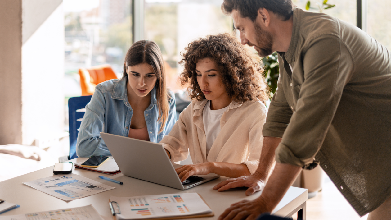 A group of teammates gather to collaborate around a computer at work