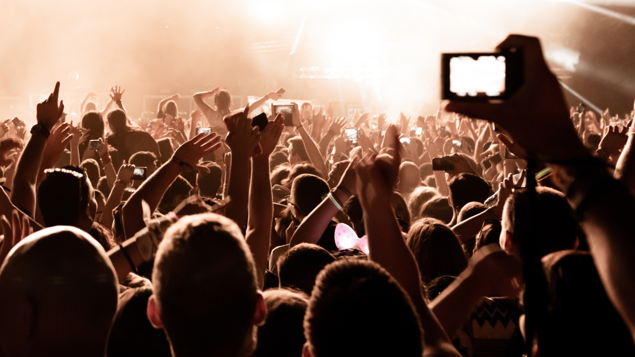 A large crowd gathers at an event, cheering enthusiastically and recording the event on their phones